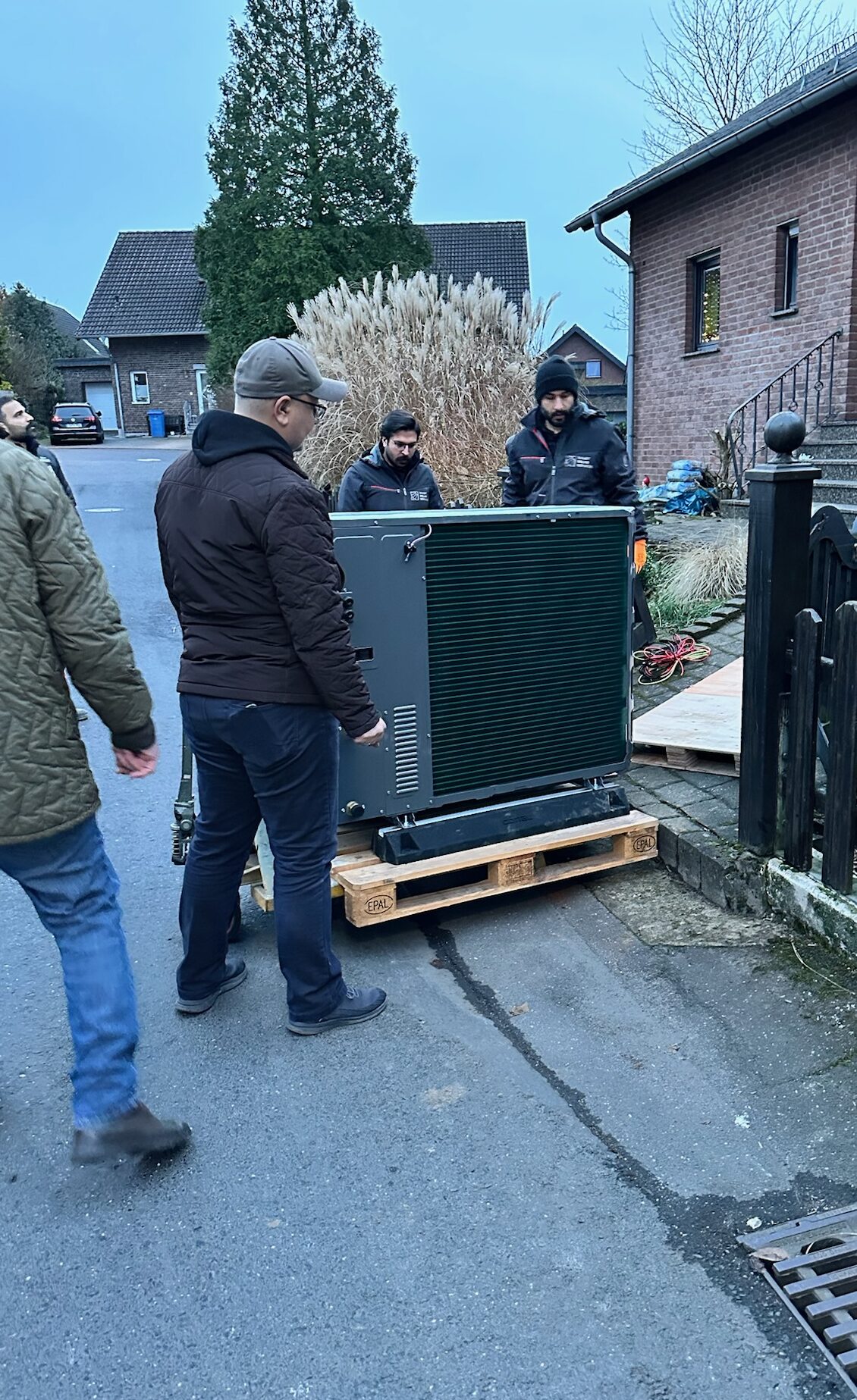 Wärmepumpe im Mietkauf – Montage vor Ort Team positioniert eine Luft-Wasser-Wärmepumpe auf Palette vor Einfamilienhaus – Mietkauf mit planbaren Raten und Service inklusive.