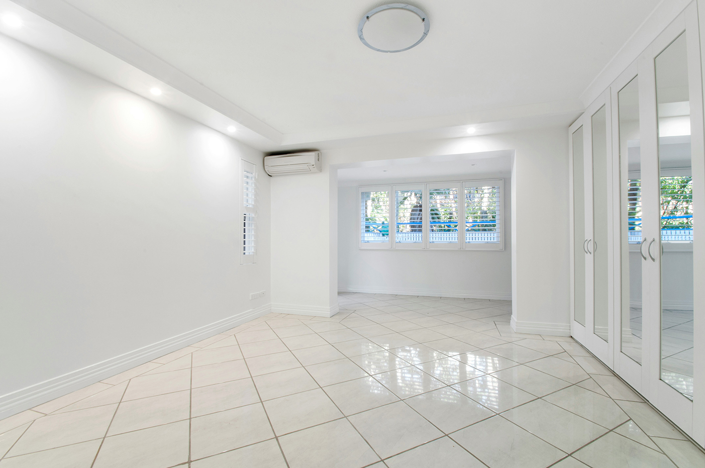 Heller Wohnraum mit wandmontierter Split-Klimaanlage; leise Kühlung, weißer Fliesenboden und Fensterläden.