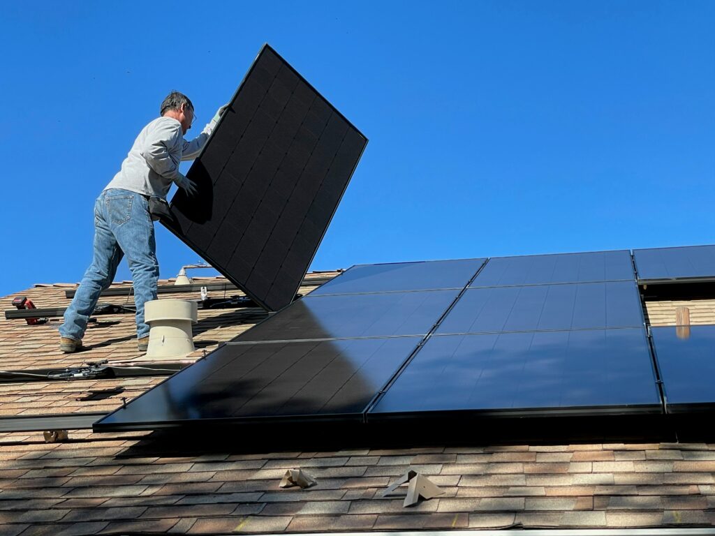 Photovoltaik im Mietkauf montieren lassen Monteur setzt ein Solarmodul auf ein Hausdach. Photovoltaik-Montage als Mietkauf mit Wartung inklusive.